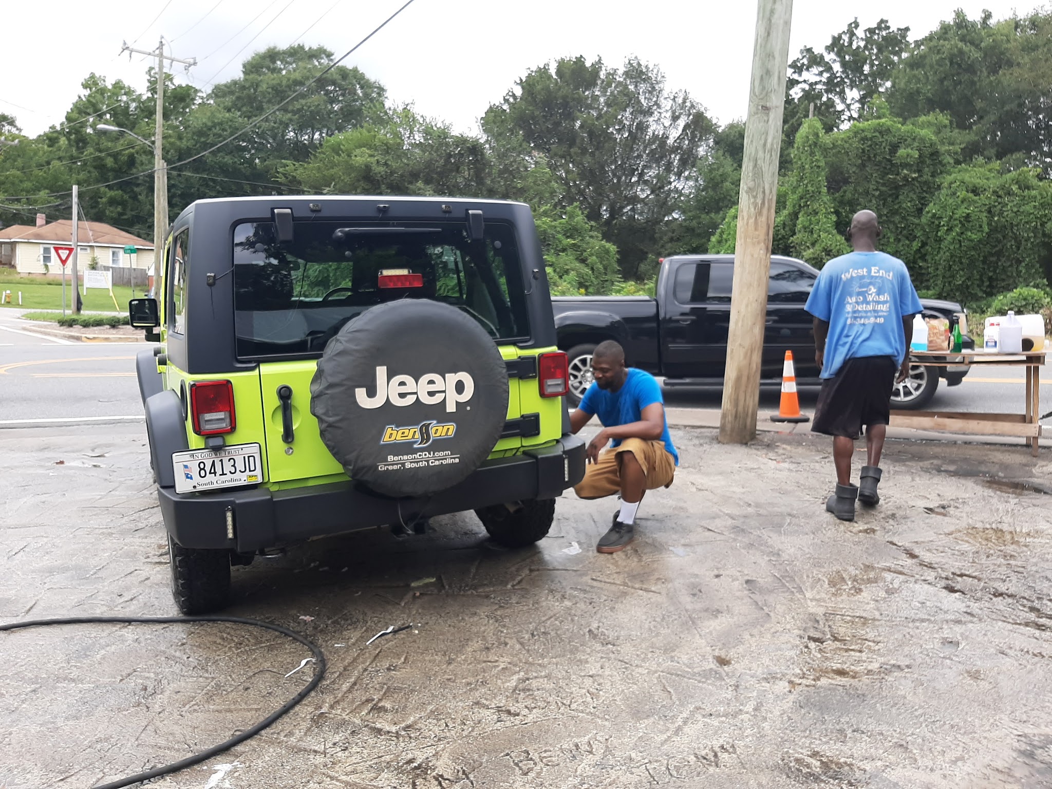 A lime green Jeep Wrangler getting its bumper wiped down while a crew member in a West End shirt walks by